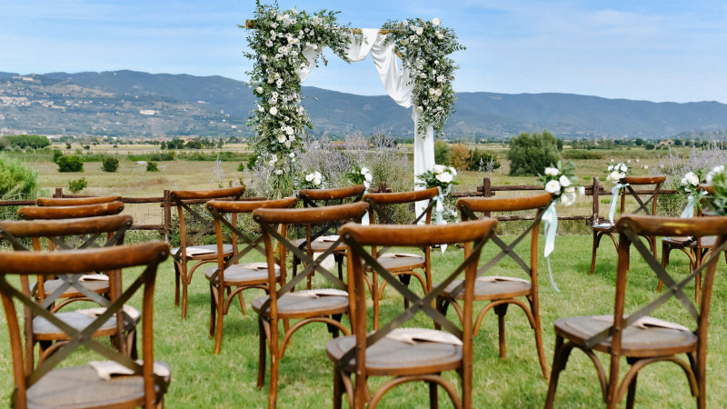 brown chiavari chairs decorated wedding archway with white flowers greenery sunny day