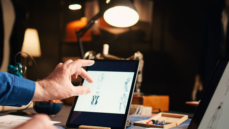 old couturier checking fashion sketches atelier working modern designs with laptop tablet experienced designer searching handmade models online needlework handheld shot